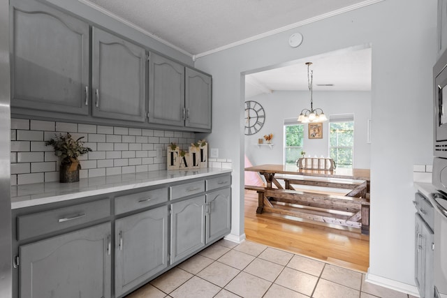 kitchen with an inviting chandelier, light hardwood / wood-style flooring, vaulted ceiling, gray cabinets, and decorative backsplash