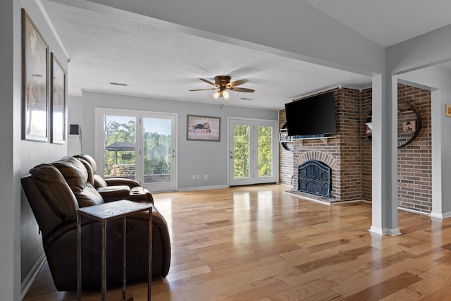 living room with a brick fireplace, light hardwood / wood-style floors, brick wall, ceiling fan, and a textured ceiling