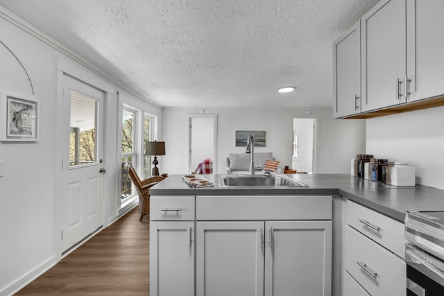 kitchen with stainless steel stove, sink, kitchen peninsula, dark wood-type flooring, and a textured ceiling