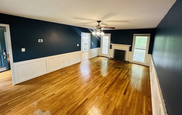 unfurnished living room featuring light wood-type flooring, a brick fireplace, and ceiling fan