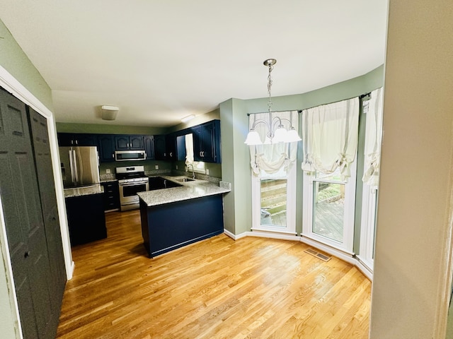 kitchen featuring a notable chandelier, stainless steel appliances, wood-type flooring, kitchen peninsula, and sink