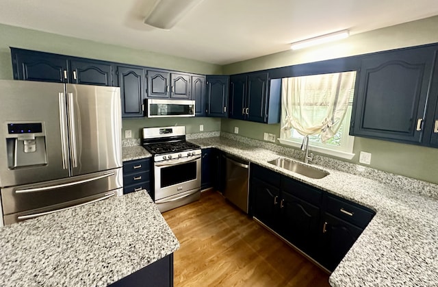 kitchen with light stone counters, stainless steel appliances, sink, and light hardwood / wood-style floors