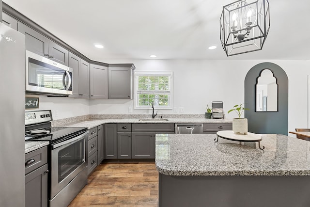 kitchen with light stone counters, stainless steel appliances, light hardwood / wood-style floors, sink, and gray cabinets