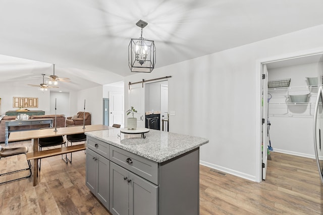 kitchen featuring a kitchen island, ceiling fan with notable chandelier, light hardwood / wood-style flooring, a barn door, and light stone counters