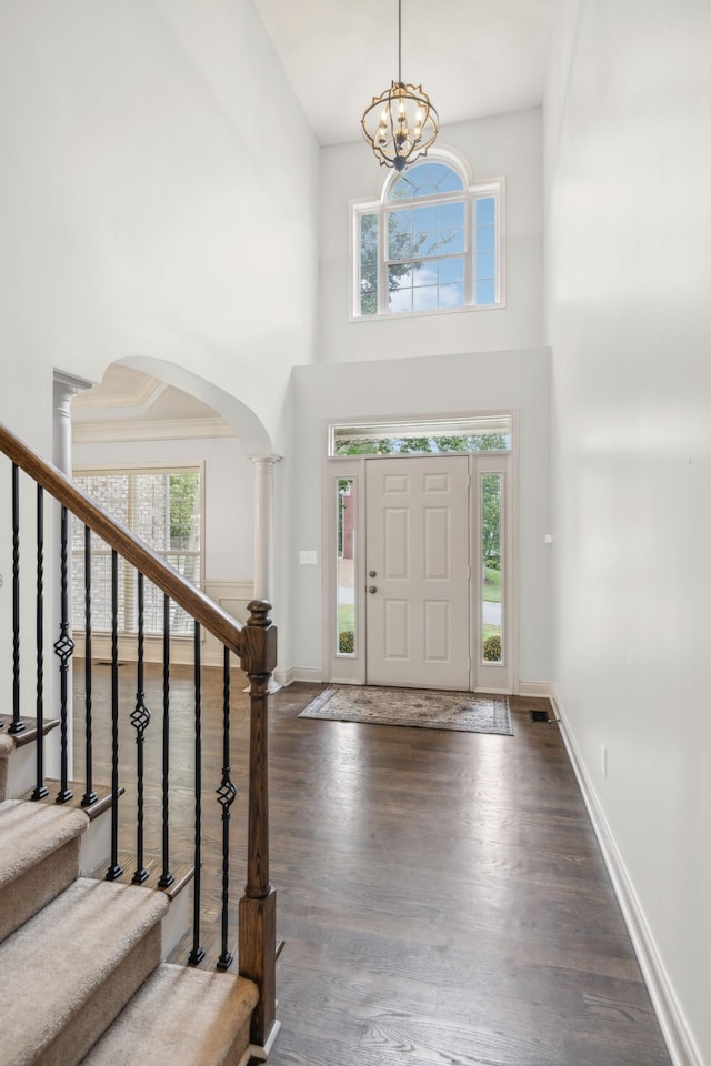 foyer with dark hardwood / wood-style floors, decorative columns, and an inviting chandelier