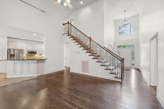 unfurnished living room with dark hardwood / wood-style flooring, ceiling fan with notable chandelier, and a high ceiling