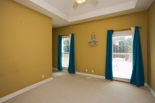 carpeted spare room featuring a tray ceiling and ceiling fan