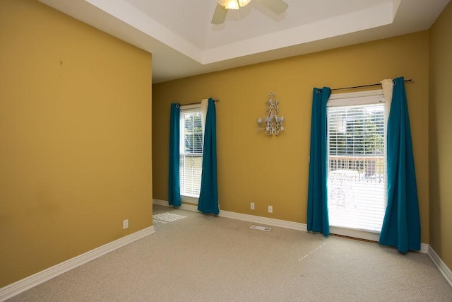 unfurnished room featuring baseboards, a tray ceiling, ceiling fan, and light carpet