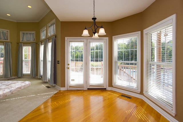 doorway to outside featuring ornamental molding, plenty of natural light, carpet flooring, and an inviting chandelier