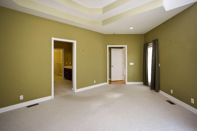 unfurnished room with baseboards, a tray ceiling, visible vents, and light colored carpet