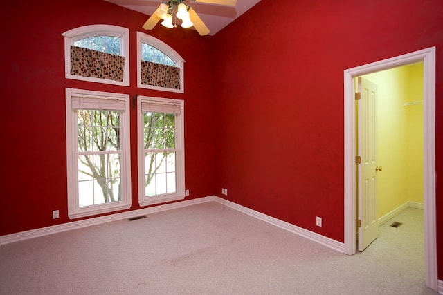 carpeted spare room with ceiling fan and a towering ceiling