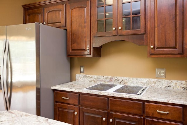 kitchen with glass insert cabinets, electric cooktop, light stone countertops, and stainless steel refrigerator with ice dispenser