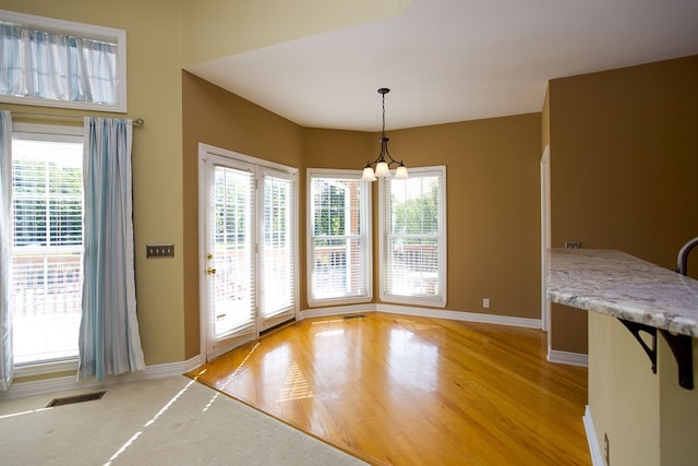 unfurnished dining area featuring light hardwood / wood-style floors, an inviting chandelier, and a healthy amount of sunlight