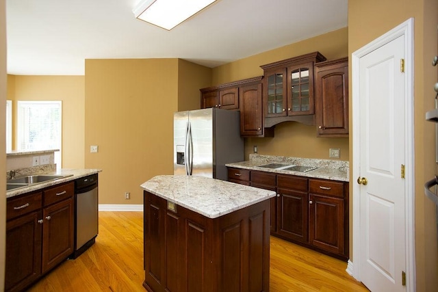kitchen featuring a sink, a kitchen island, glass insert cabinets, stainless steel appliances, and light wood-style floors