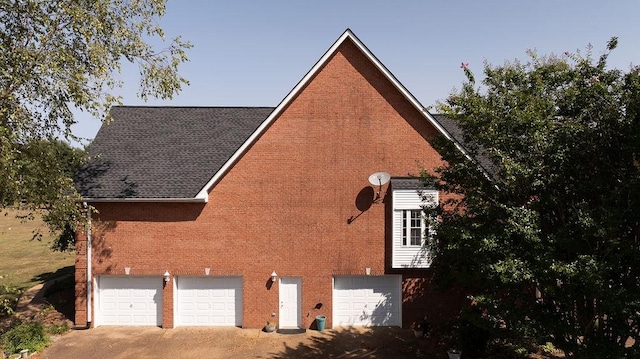 view of home's exterior featuring driveway, a garage, brick siding, and roof with shingles