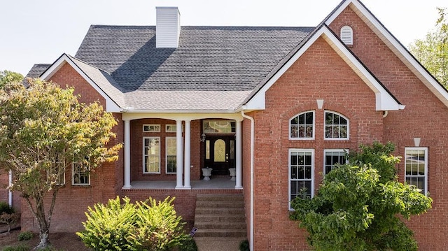 back of house with brick siding, a chimney, and covered porch