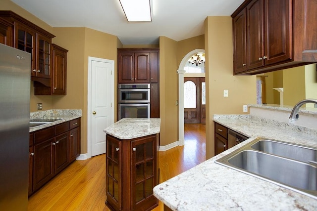 kitchen with light wood-type flooring, a sink, arched walkways, appliances with stainless steel finishes, and glass insert cabinets