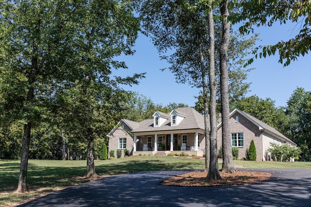 cape cod-style house featuring a porch, brick siding, a front yard, and aphalt driveway