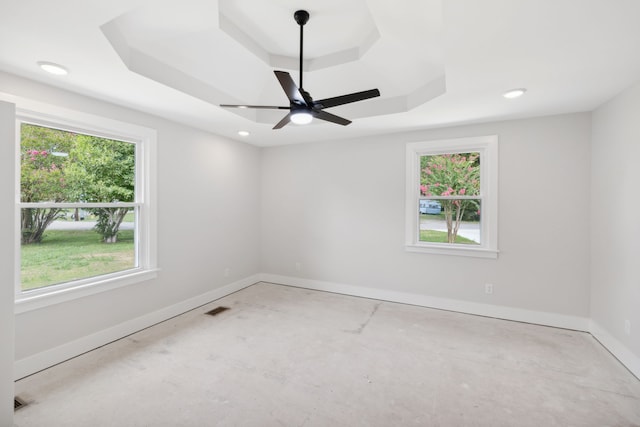 empty room with a tray ceiling, a healthy amount of sunlight, and ceiling fan