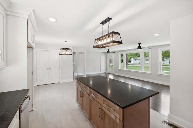 kitchen with decorative light fixtures, light hardwood / wood-style floors, ceiling fan, a kitchen island, and stainless steel dishwasher