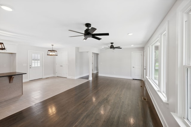 unfurnished living room featuring ceiling fan with notable chandelier, dark hardwood / wood-style flooring, and a healthy amount of sunlight