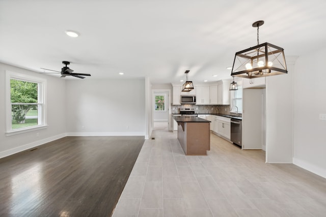 kitchen with white cabinets, hanging light fixtures, a center island, ceiling fan with notable chandelier, and stainless steel appliances