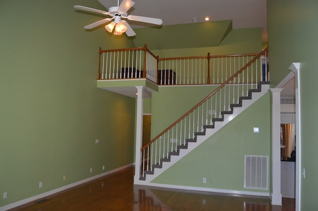 staircase with ceiling fan, a towering ceiling, and hardwood / wood-style flooring