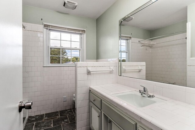 bathroom with a tile shower, tile walls, and vanity