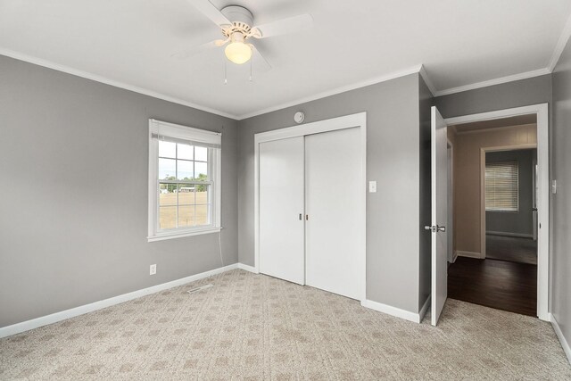 unfurnished bedroom featuring ceiling fan, a closet, light carpet, and crown molding