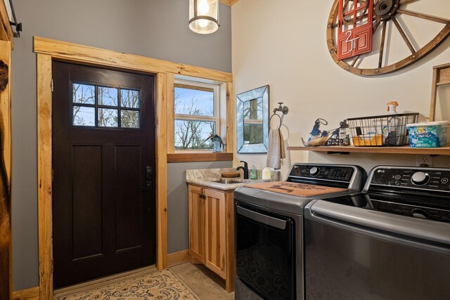 clothes washing area with washing machine and clothes dryer, cabinets, and sink