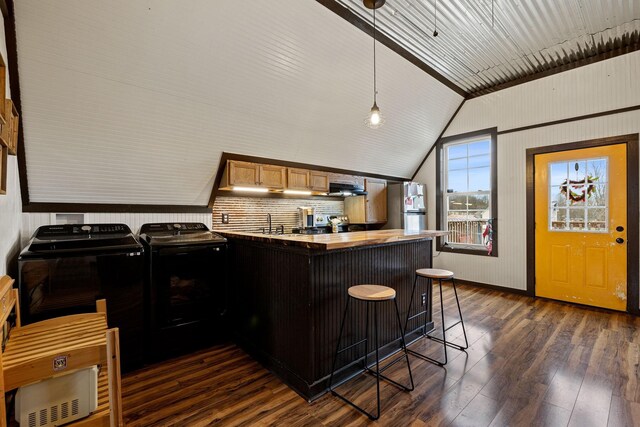 kitchen with separate washer and dryer, dark hardwood / wood-style flooring, kitchen peninsula, lofted ceiling, and a breakfast bar area