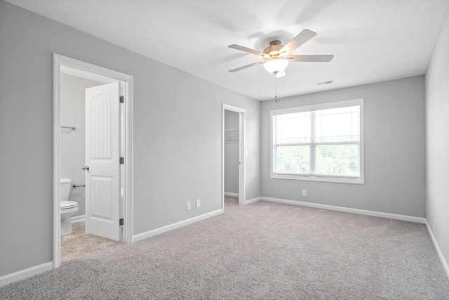 unfurnished bedroom featuring a spacious closet, visible vents, baseboards, carpet floors, and ensuite bathroom