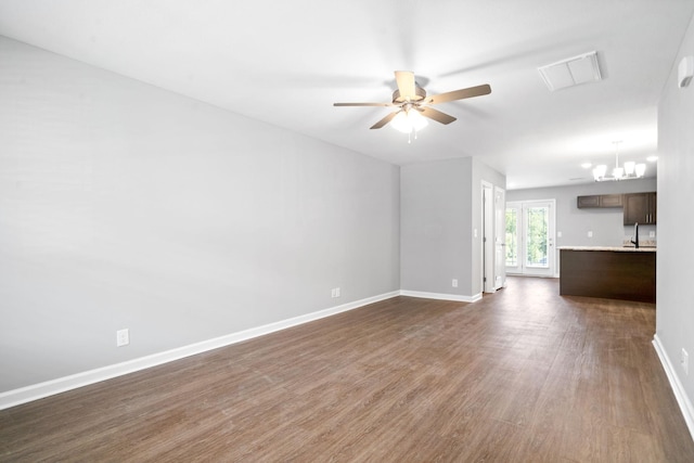 unfurnished living room with dark wood finished floors, ceiling fan with notable chandelier, and baseboards