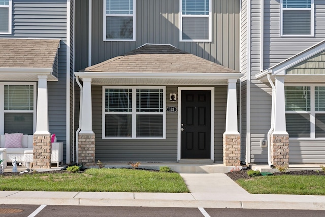 entrance to property with a porch, stone siding, board and batten siding, and a shingled roof