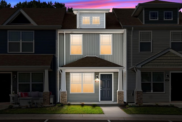 townhome / multi-family property with stone siding, covered porch, board and batten siding, and a shingled roof