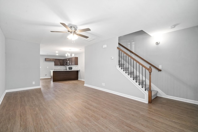 unfurnished living room with wood finished floors, stairway, ceiling fan with notable chandelier, and baseboards