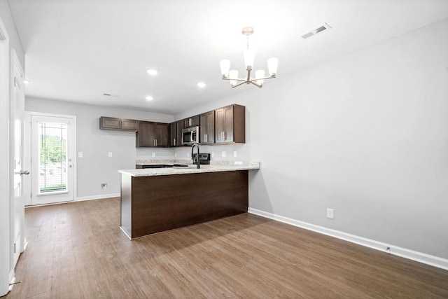 kitchen with wood finished floors, an inviting chandelier, a peninsula, dark brown cabinetry, and stainless steel microwave