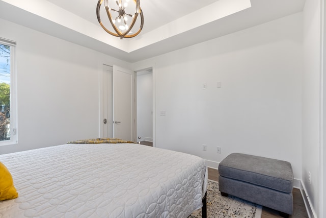 bedroom featuring a tray ceiling, hardwood / wood-style flooring, and an inviting chandelier