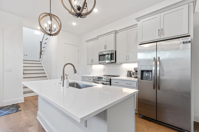 kitchen featuring decorative light fixtures, stainless steel appliances, an inviting chandelier, sink, and a center island with sink