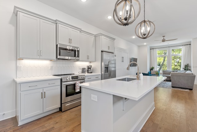 kitchen featuring ceiling fan with notable chandelier, light hardwood / wood-style flooring, stainless steel appliances, sink, and a center island with sink