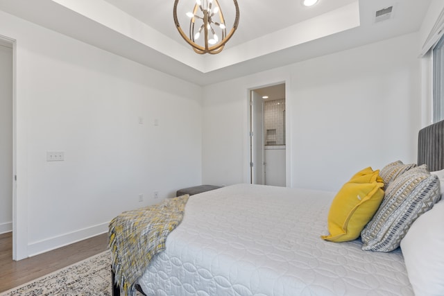 bedroom featuring ensuite bath, a raised ceiling, a chandelier, and light hardwood / wood-style floors