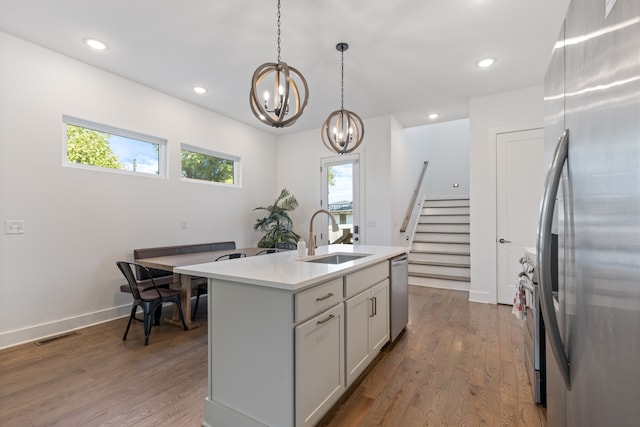 kitchen featuring pendant lighting, stainless steel appliances, sink, hardwood / wood-style flooring, and a center island with sink