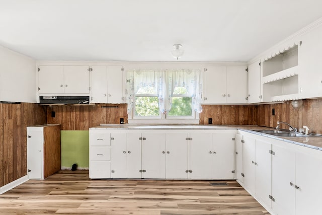 kitchen featuring crown molding, wood walls, sink, white cabinets, and light hardwood / wood-style floors