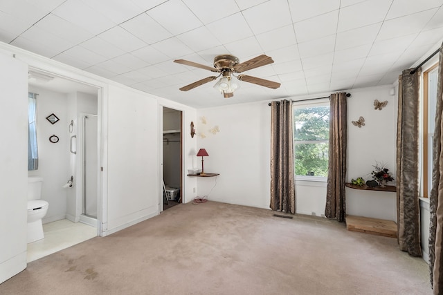 unfurnished bedroom with light colored carpet, a walk in closet, a closet, ceiling fan, and connected bathroom