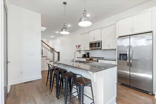 kitchen featuring light hardwood / wood-style flooring, stainless steel appliances, sink, a center island with sink, and white cabinets