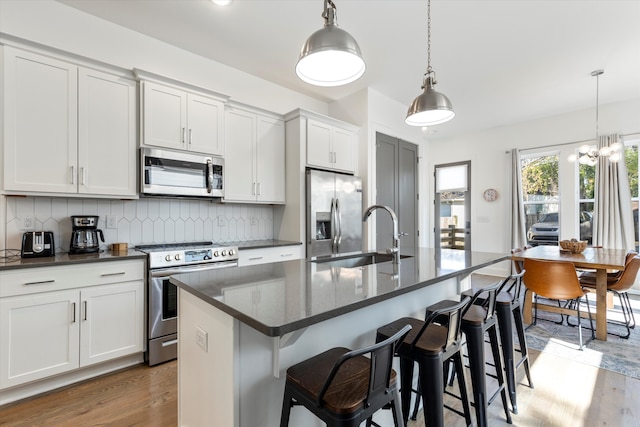 kitchen with light wood-type flooring, stainless steel appliances, sink, a center island with sink, and tasteful backsplash