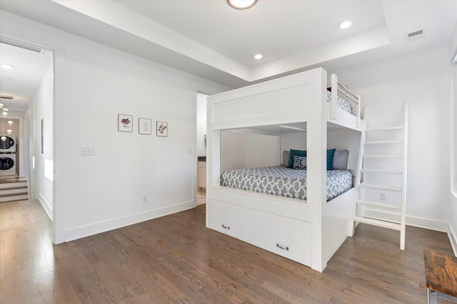 bedroom with dark wood-type flooring, a tray ceiling, and stacked washer and dryer