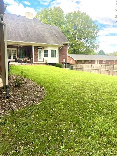 rear view of house with a yard, fence, brick siding, a chimney, and a shingled roof