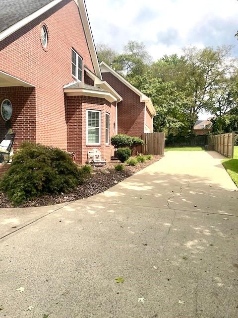 view of side of home featuring concrete driveway, brick siding, and fence