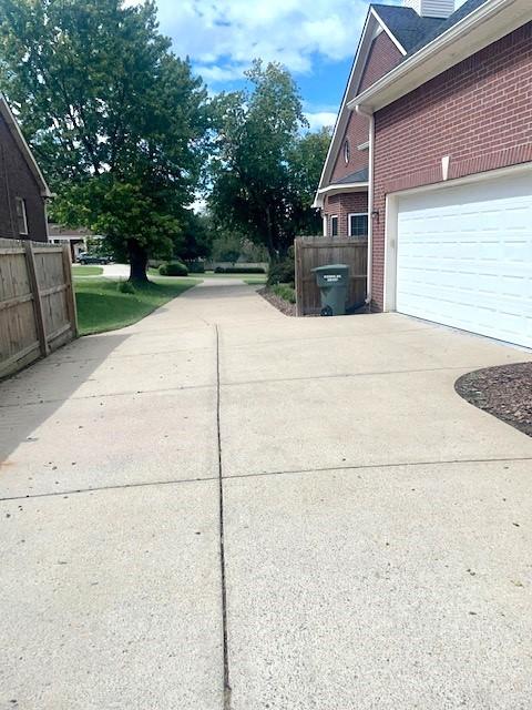 view of side of home with brick siding, fence, and driveway